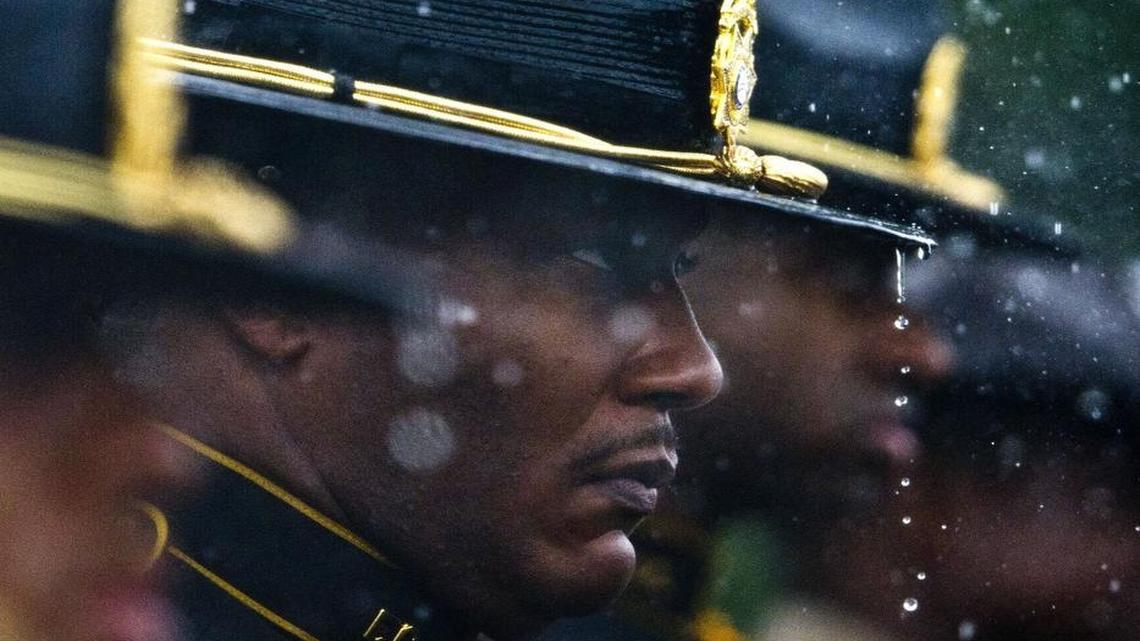 Rain water drips from Fulton County sheriff’s honor guard member Sgt. Randell Lattimore’s campaign hat as he stands at attention at the graveside service for Eastman police officer Tim Smith in August.
