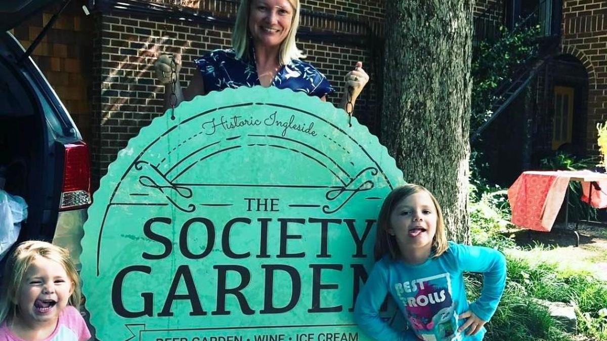 Meagan Evans, co-owner of The Society Garden, with daughters Iris and Ella holding the business sign and logo.