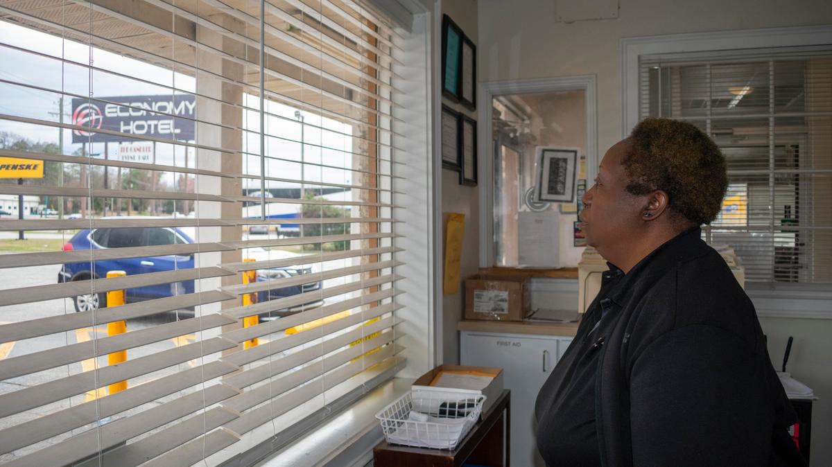 Imogene Patterson peers through the blinds behind the check-in desk at Economy Hotel on Pio Nono. She said she sometimes holds her breath watching some of the hotel guests trying to cross the five lanes of Pio Nono Avenue to get to the Circle K convenience store.