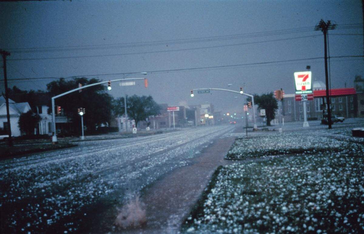 Large hail collects on streets and grass during severe thunderstorm. Larger stones appear to be nearly 2 to 3 inches in diameter.