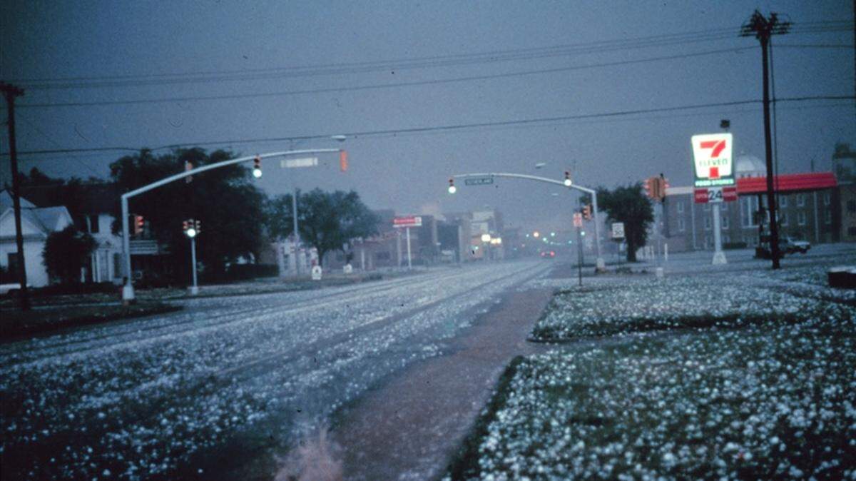 Large hail collects on streets and grass during severe thunderstorm. Larger stones appear to be nearly 2 to 3 inches in diameter.