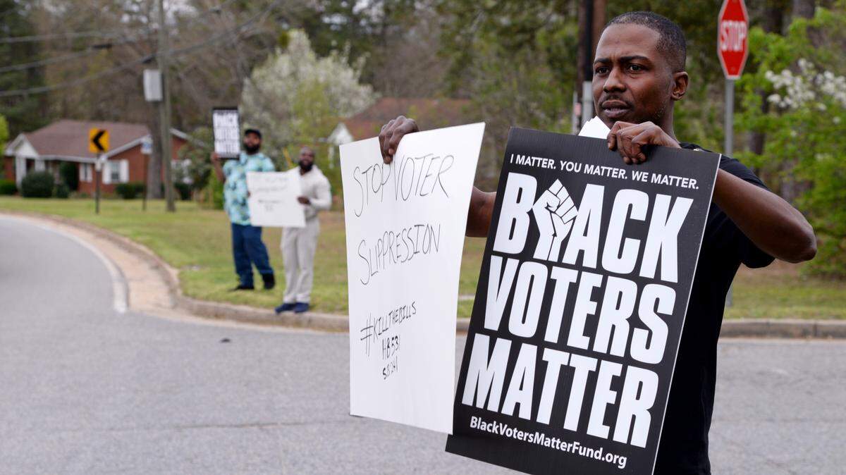 L. J. Malone holds signs at the entrance of the Coca-Cola Bottling Co. on Rocky Creek Road as part of a Black Voters Matter campaign to hold large corporations accountable. Coca-Cola and many other companies pledged to support racial equity during the summer of protests in 2020 following the deaths of George Floyd, Breonna Taylor and Ahmaud Arbery. Black Voters Matter is trying to get those same companies to help them fight voter suppression in Georgia.