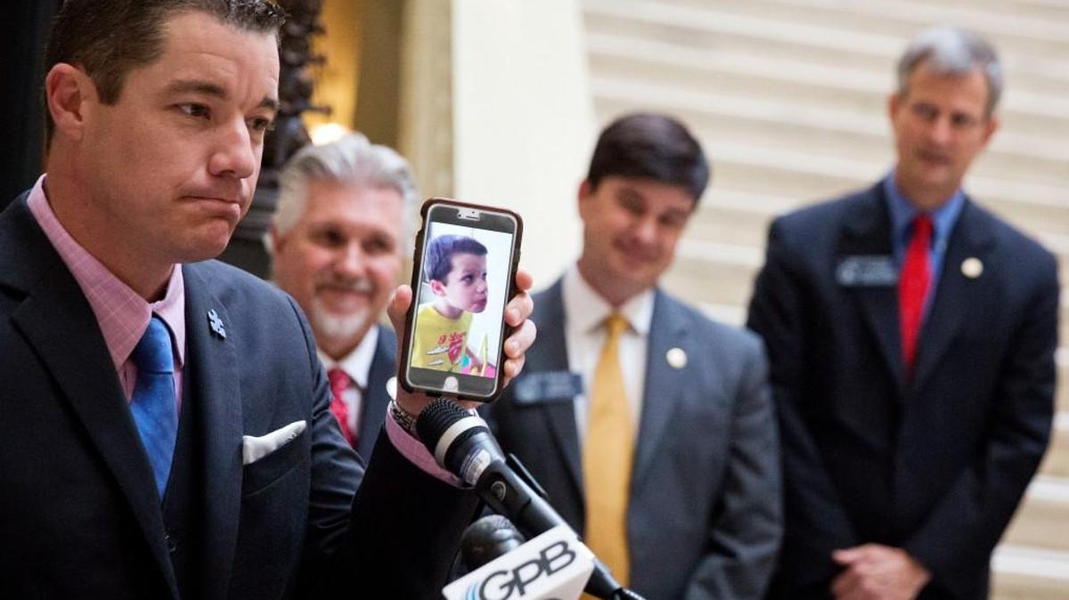 Dale Jackson shows a video of his eight-year-old autistic son Colin saying his first word after being treated with cannabis oil as state lawmakers look on during a press conference at the Capitol in Atlanta, Tuesday, March 28. Two years after Georgia legalized medical marijuana, lawmakers are opening the popular program to more patients. The House approved a bill Tuesday that would add six new diagnoses to the list of qualifying conditions for medical cannabis oil, including autism, AIDS, Tourette's syndrome, and Alzheimer's disease.