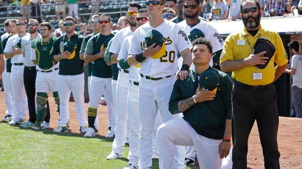 Oakland Athletics' Mark Canha (20) places his hand on the shoulder of Bruce Maxwell as Maxwell takes a knee during the national anthem prior to a baseball game against the Texas Rangers in Oakland, Calif. What began more than a year ago with a lone NFL quarterback protesting police brutality against minorities by kneeling silently during the national anthem before games has grown into a roar with hundreds of players sitting, kneeling, locking arms or remaining in locker rooms, their reasons for demonstrating as varied as their methods.
