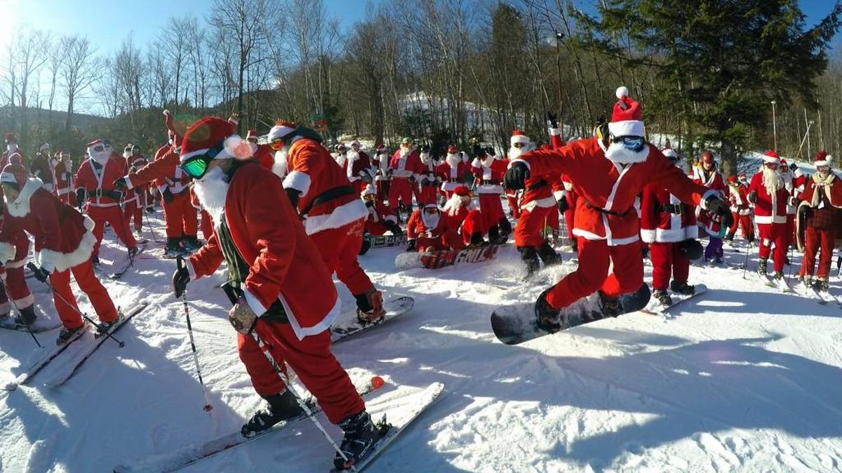 A snowboarder, right, gets a jump start as 160 Santas head down a slope at Sunday River during the ski resort's 18th annual Santa Sunday event, Sunday, Dec. 3, 2017, in Newry, Maine. The Santas raised $2,500 for the Sunday River Community Fund, a fund that benefits non-profits in area communities.