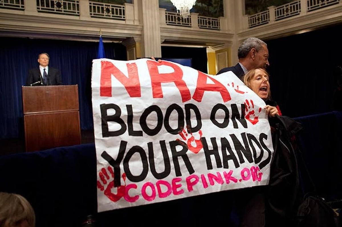 An activist is led away by security after protesting during a statement by NRA CEO Wayne LaPierre, left, during a news conference in response to the Connecticut school shooting in 2012.