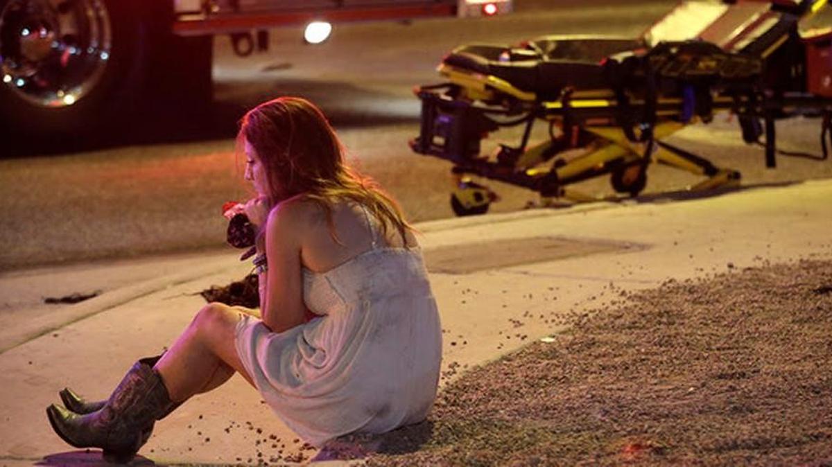 A woman sits on a curb at the scene of a shooting outside of a music festival along the Las Vegas Strip, Monday, Oct. 2, 2017, in Las Vegas. Multiple victims were being transported to hospitals after a shooting late Sunday at a music festival on the Las Vegas Strip.