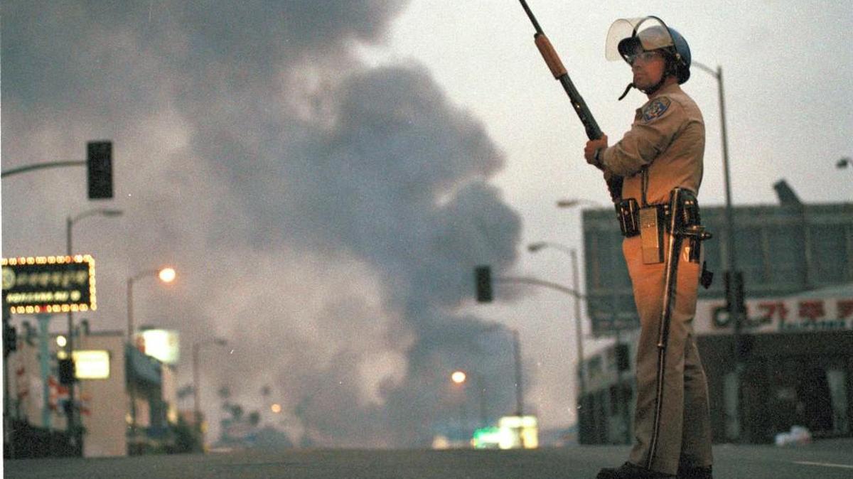 A California Highway Patrol officer stands guard at Ninth Street and Vermont Avenue in Los Angeles as smoke rises from a fire further down the street, April 30, 1992. It was the second day of unrest in Los Angeles following the acquittal of four Los Angeles police officers in the Rodney King beating case.