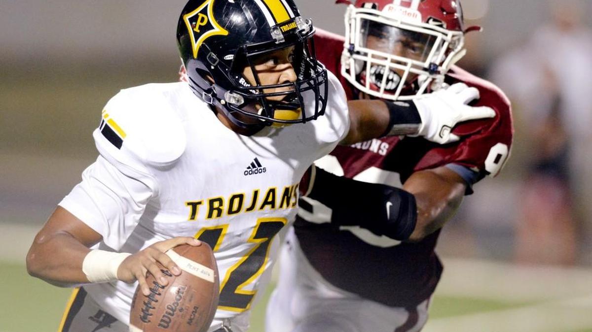 Peach County quarterback Antonio Gilbert (12), avoiding a sack by Warner Robins' Bobby Kelly (99) during their game Friday night, will lead the Trojans into Perry.