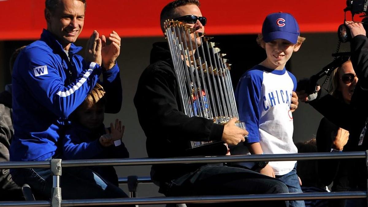 Chicago Cubs president of baseball operations Theo Epstein holds the Commissioner's Trophy while his son, Jack, right, and Chicago Cubs vice president of baseball operations and general manager Jed Hoyer, left, look on during a parade outside Wrigley Field honoring the World Series champions Friday, Nov. 4, 2016, in Chicago.