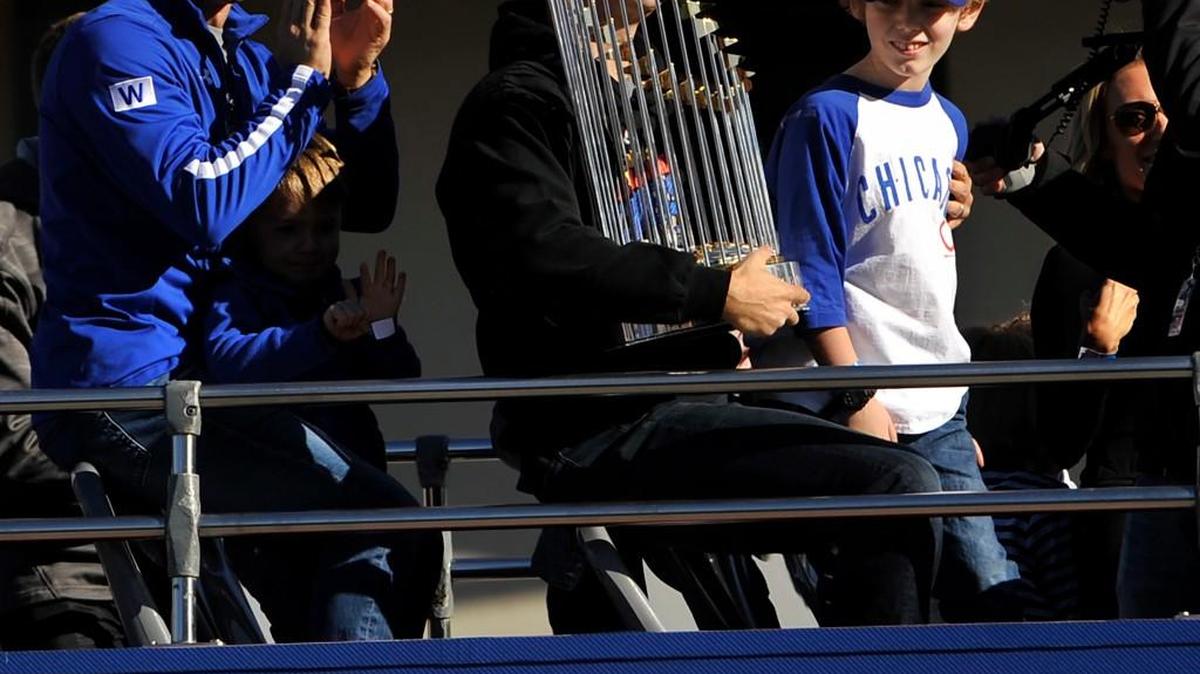 Chicago Cubs president of baseball operations Theo Epstein holds the Commissioner's Trophy while his son, Jack, right, and Chicago Cubs vice president of baseball operations and general manager Jed Hoyer, left, look on during a parade outside Wrigley Field honoring the World Series champions.